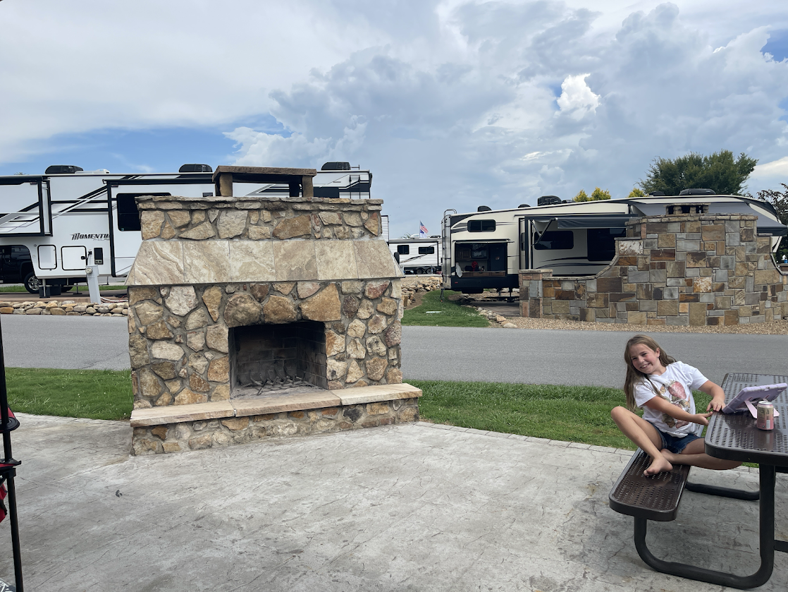 Stone fireplace in the foreground with RVs and child sitting nearby.