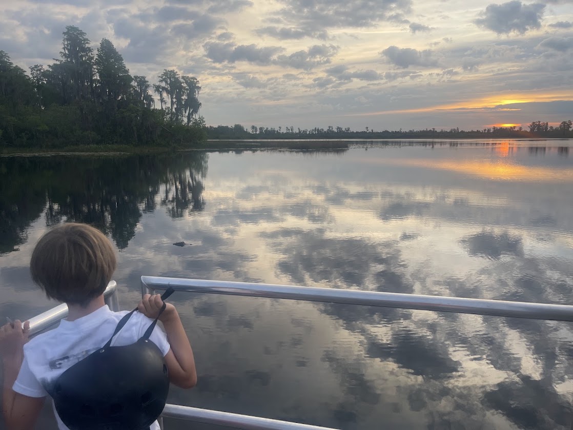 Child observing the sunset over tranquil water from a railing.
