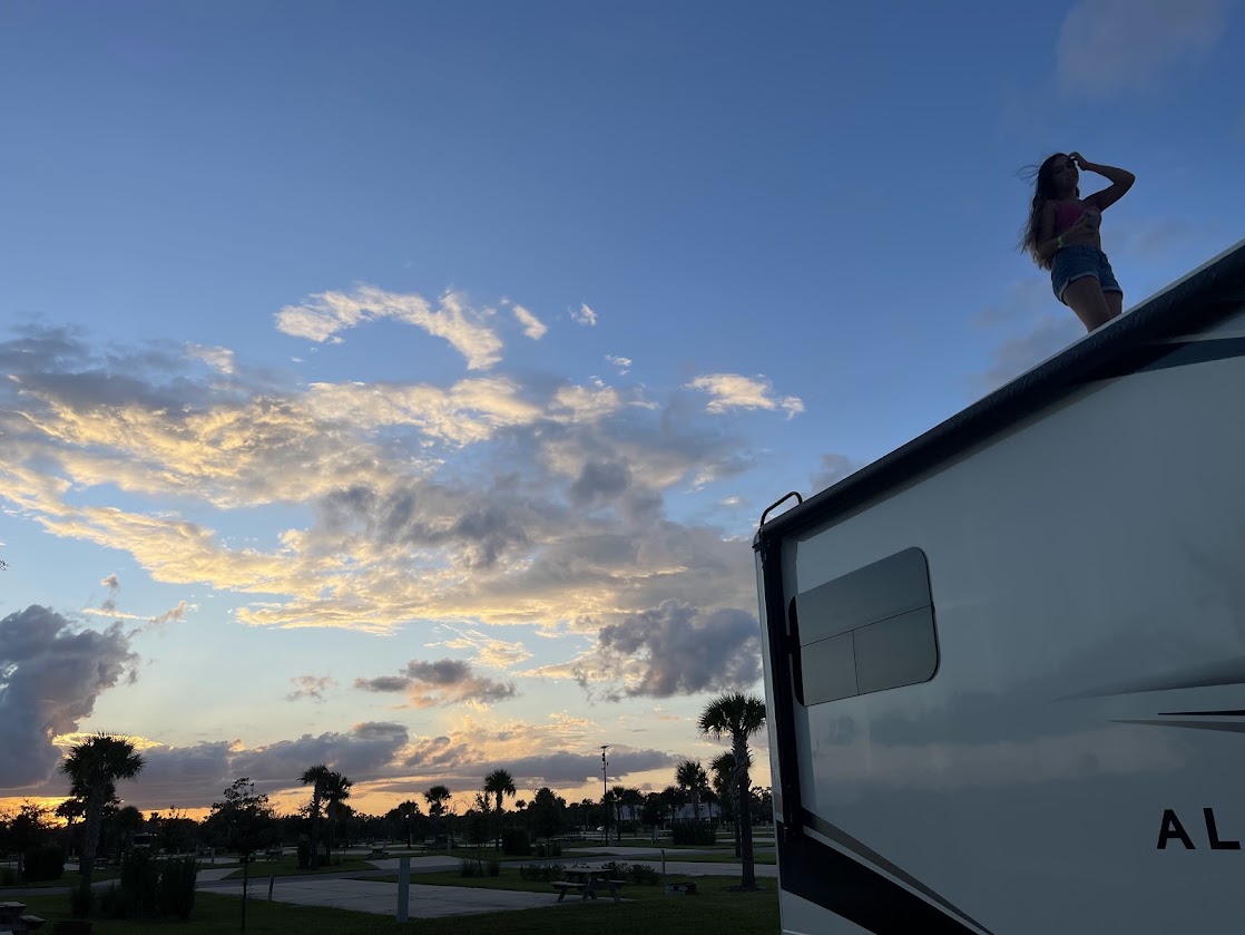 Silhouette of a girl standing on top of an RV against a colorful sunset.