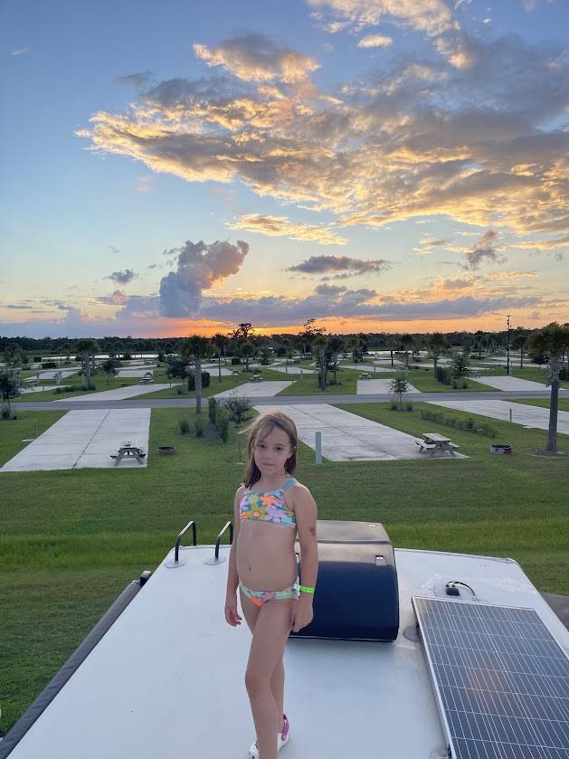 A girl standing on an RV roof at sunset, overlooking the RV park.