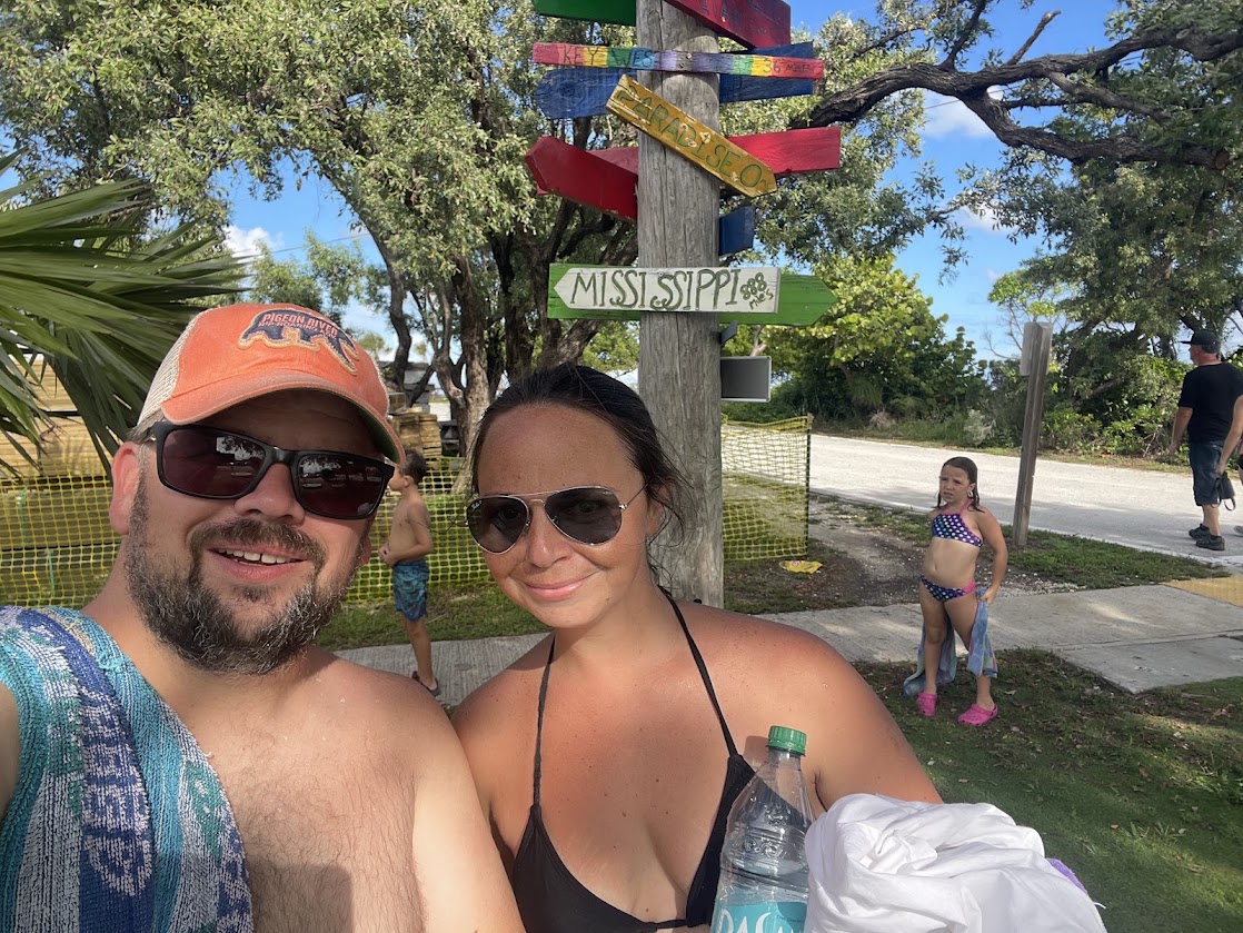 Two adults smiling with children in swimwear near directional sign.