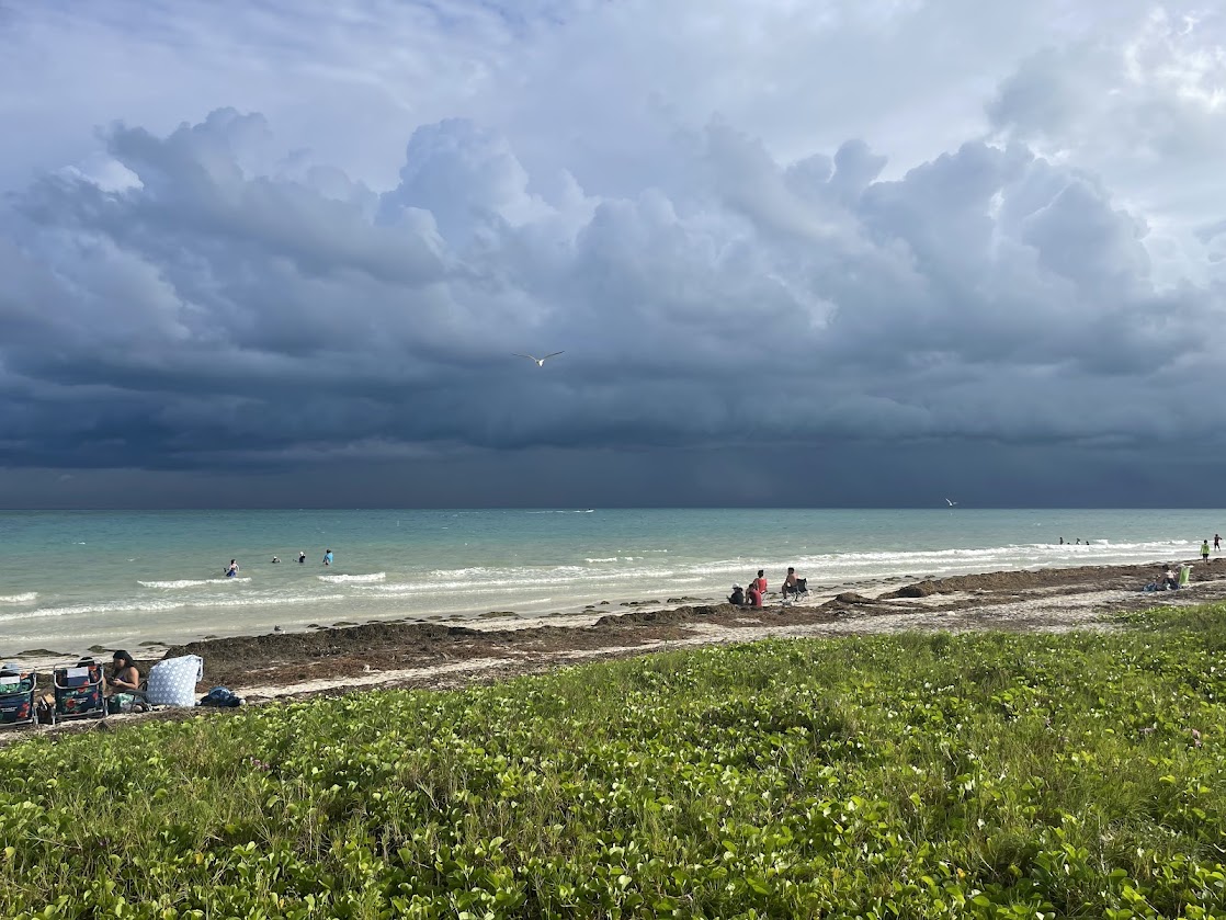 Cloudy beach scene with people swimming and sitting along the shore.