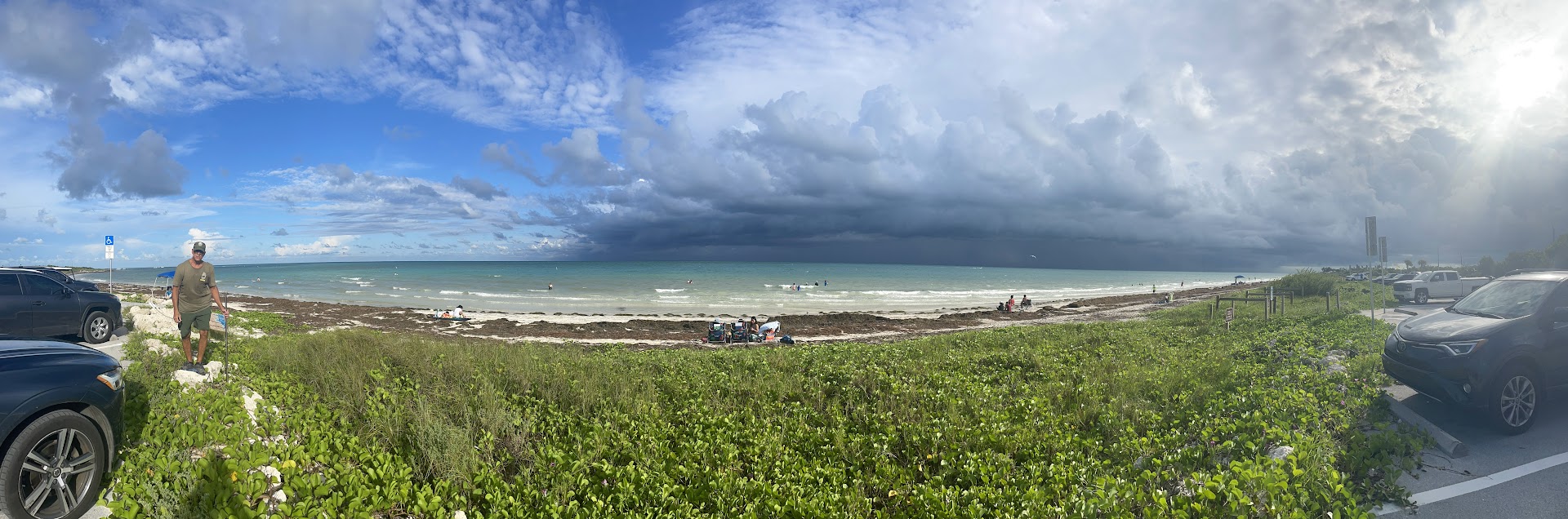 Panoramic view of beach with dark clouds and people enjoying the water.