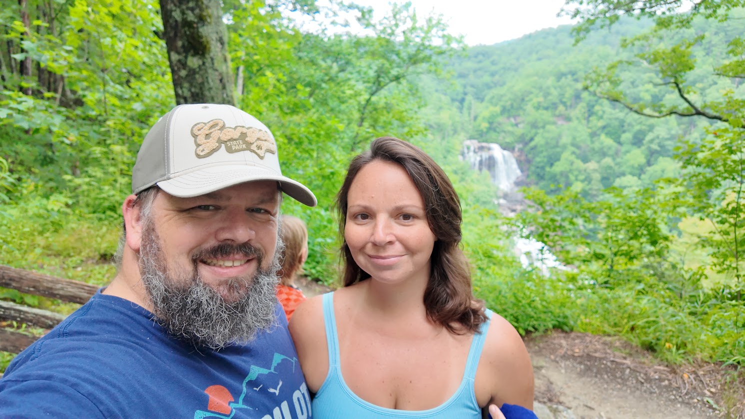 A couple posing for a photo in front of Whitewater Falls and lush greenery.
