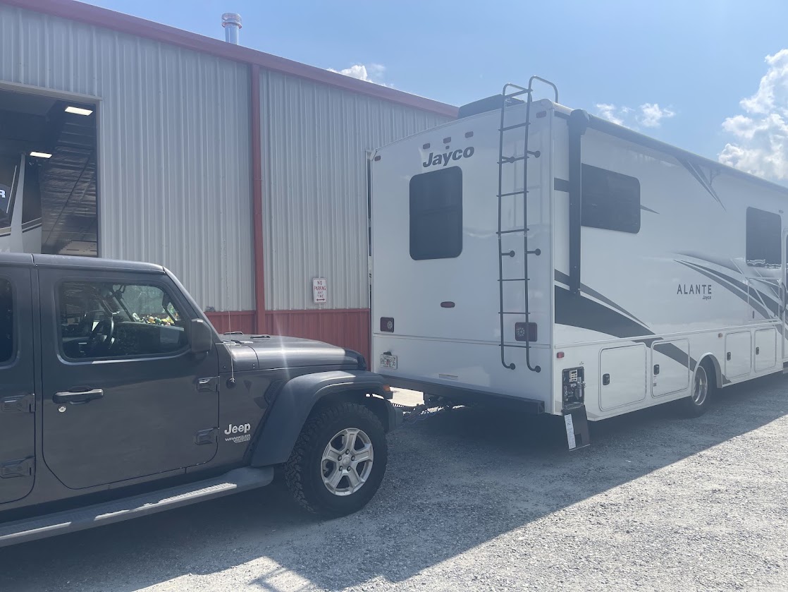 A Jeep parked next to a Class A motorhome at an RV repair shop.