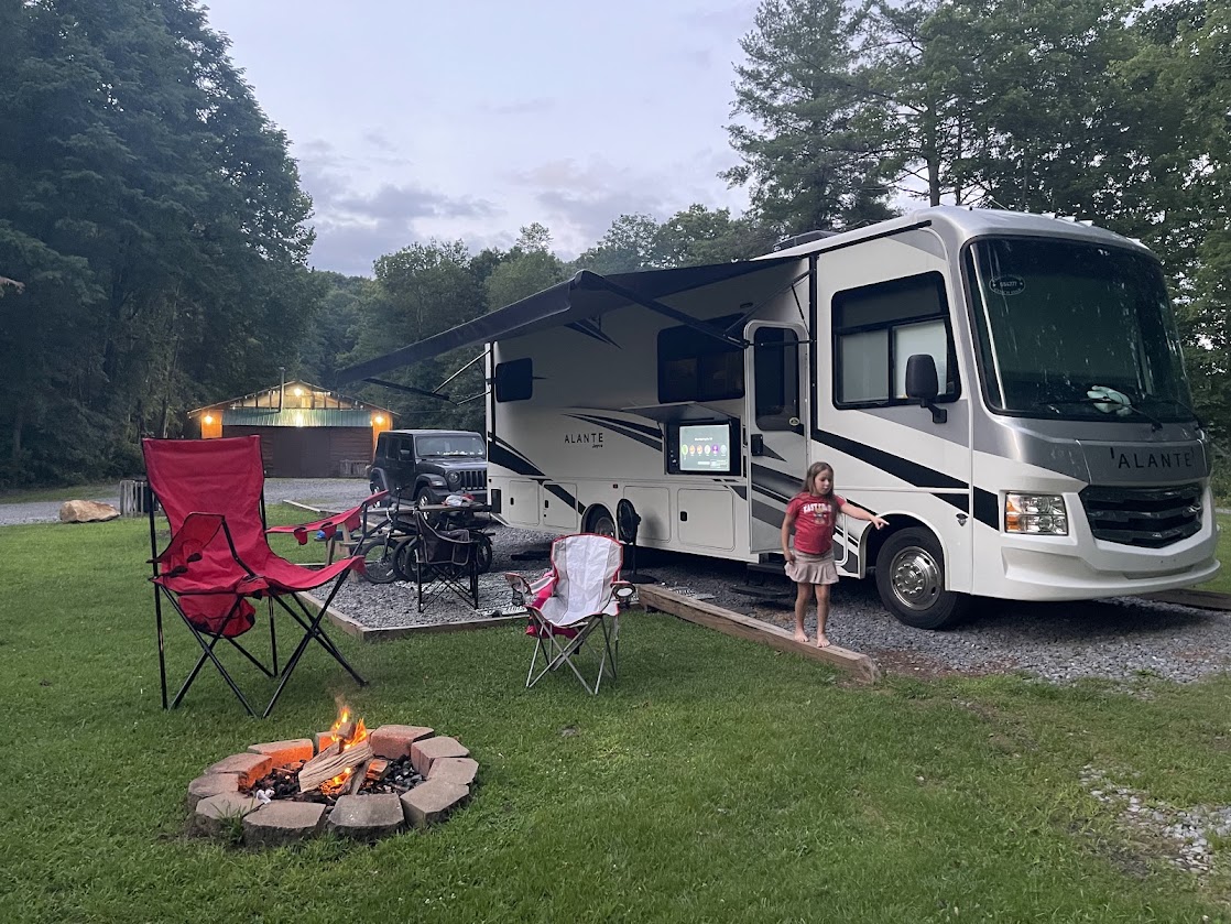 RV parked next to a campfire setup and picnic area at dusk.