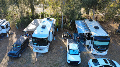 Two RVs with awnings, a black Jeep, and a white car parked nearby.