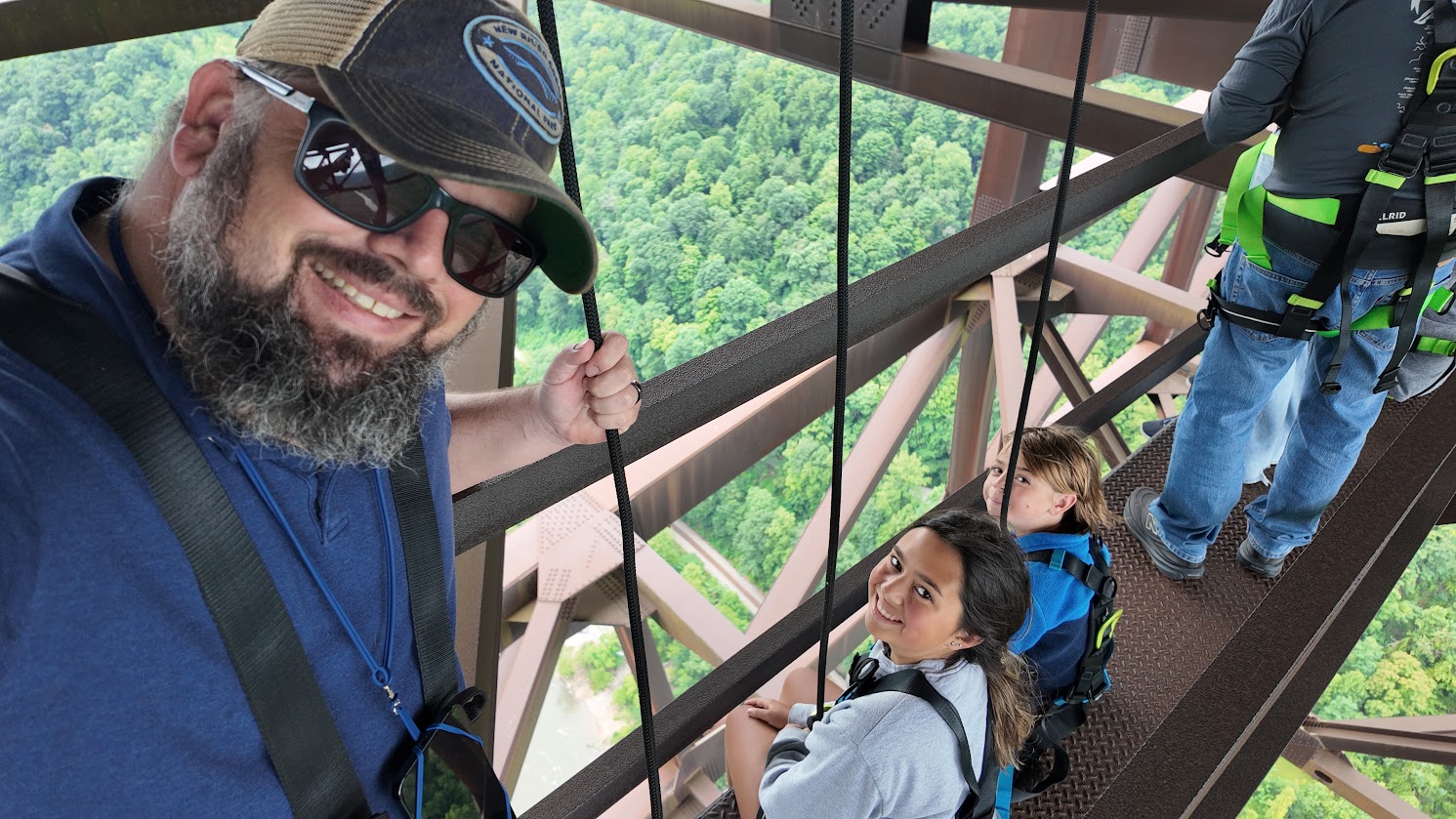 Three individuals in harnesses stand on a metal structure overlooking the gorge.