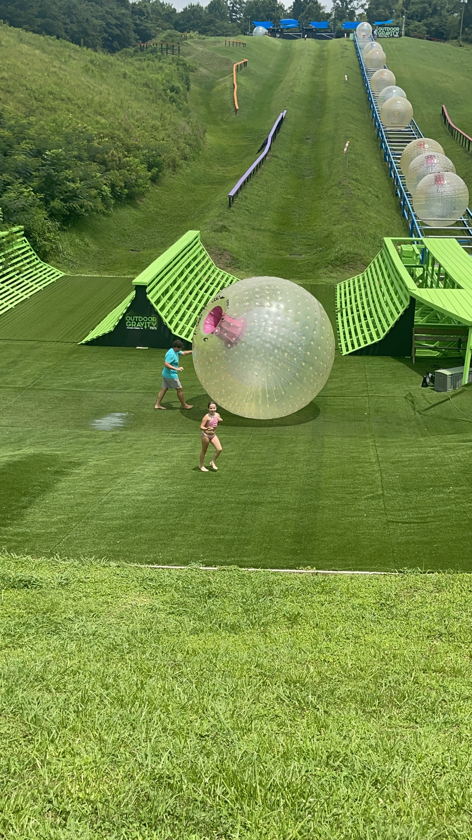 A child runs on a grassy slope near inflatable zorb balls.