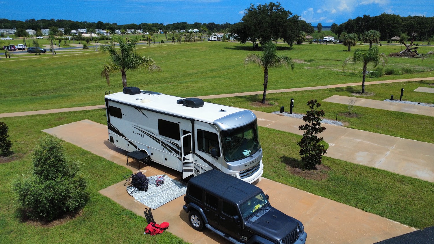 Aerial view of an RV and a Jeep parked on a grassy site.