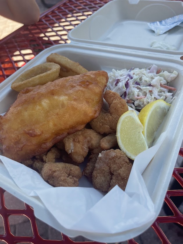 A to-go container with fried fish, shrimp, coleslaw, and lemon.