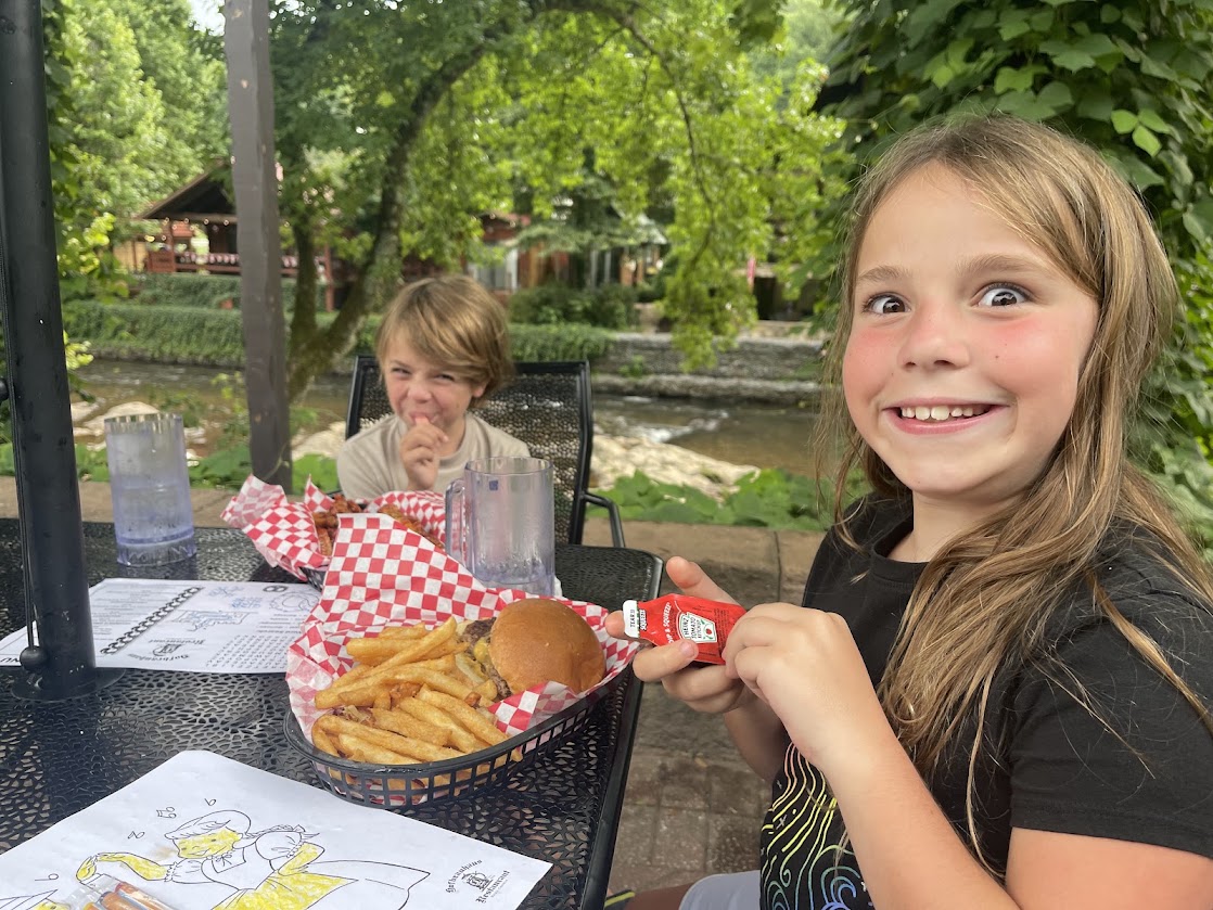 A child smiling at the camera with a burger and fries on the table.