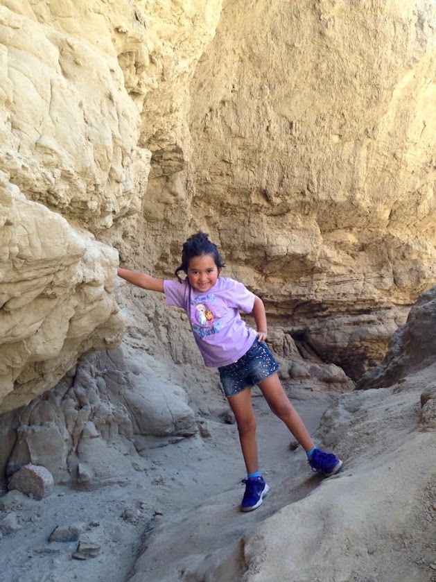 A child posing with one hand on a canyon wall while smiling.