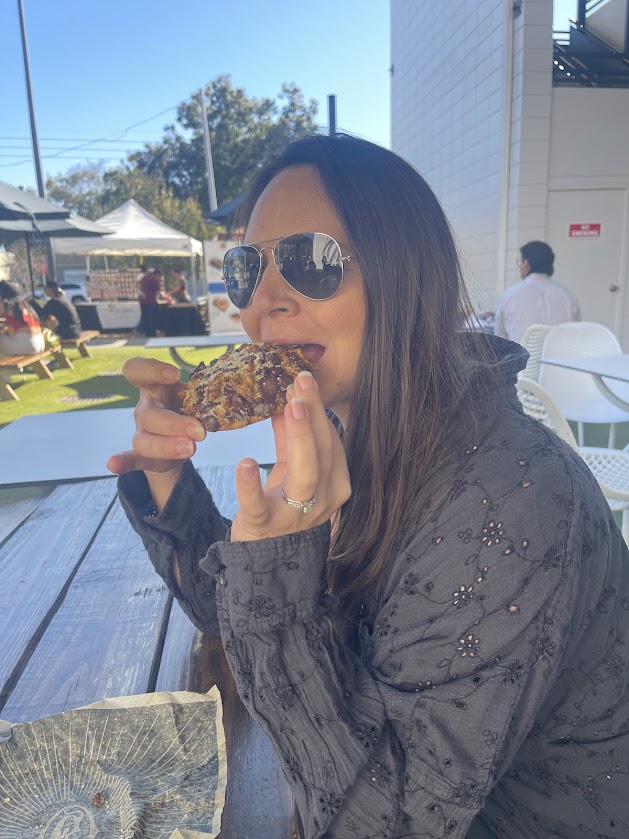 An adult woman poses with a dessert, smiling while wearing sunglasses.