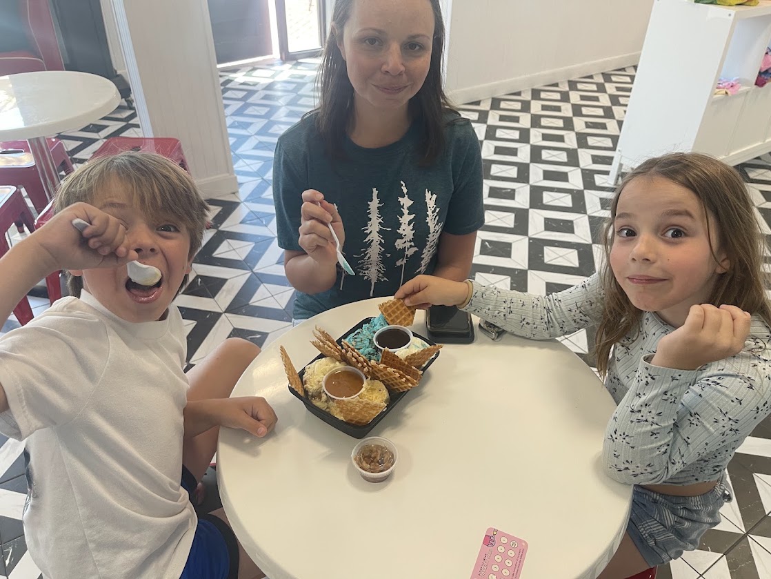 Two children and an adult enjoying ice cream at a table with a geometric floor.