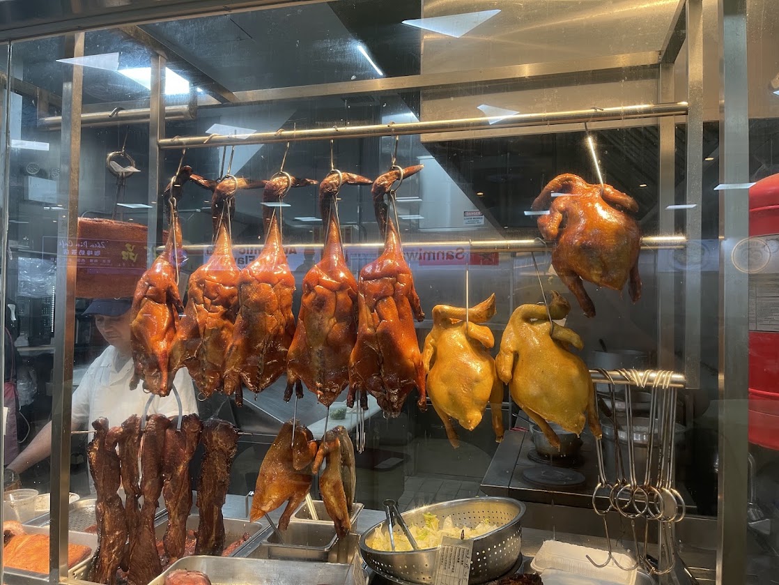 Roasted ducks hanging in a glass display at Mott Eatery.