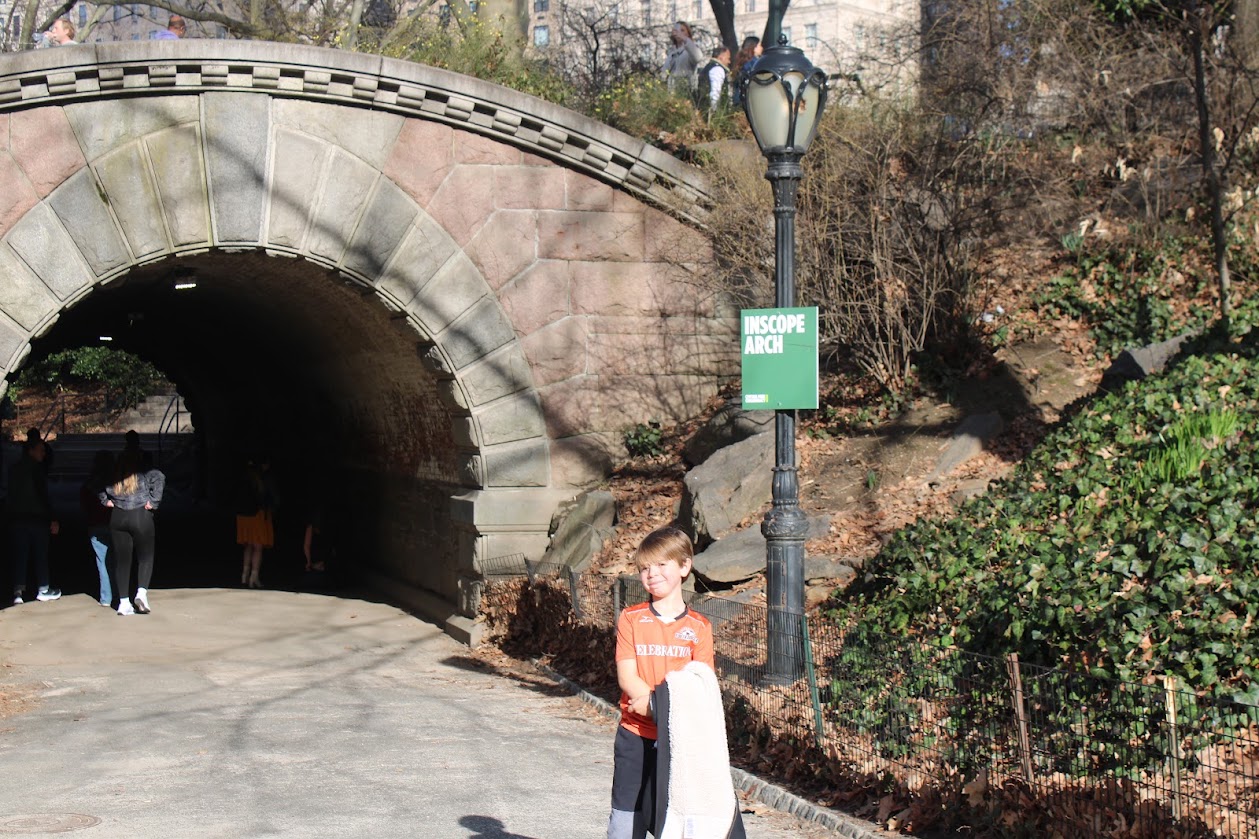 A child stands under an arch in Central Park, with a sign visible.