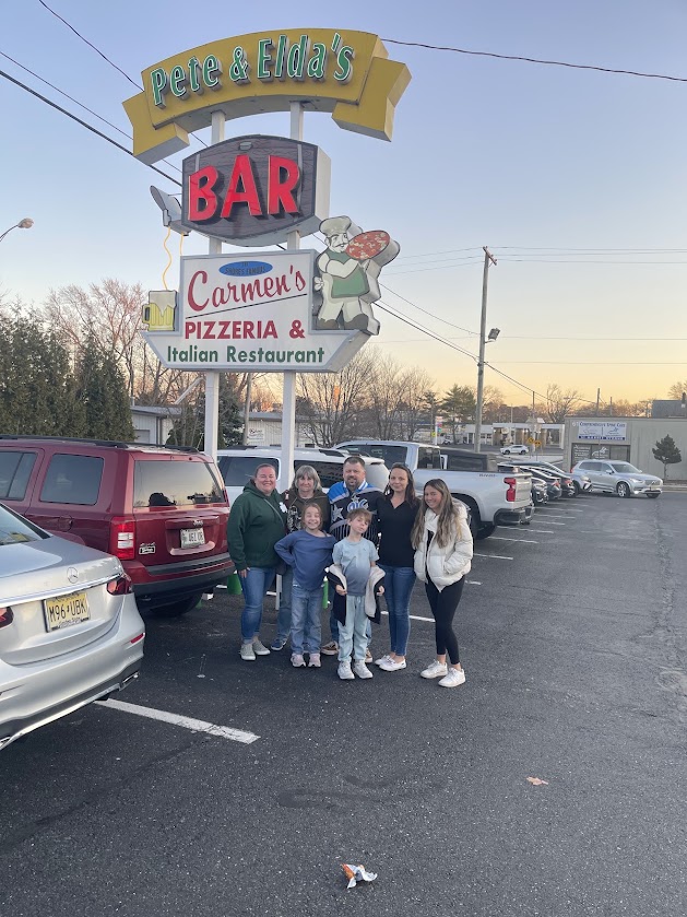 A group of six people stands in front of Carmen's Pizza restaurant sign.