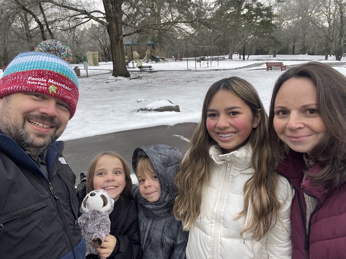 A smiling family poses together in a snowy park setting.