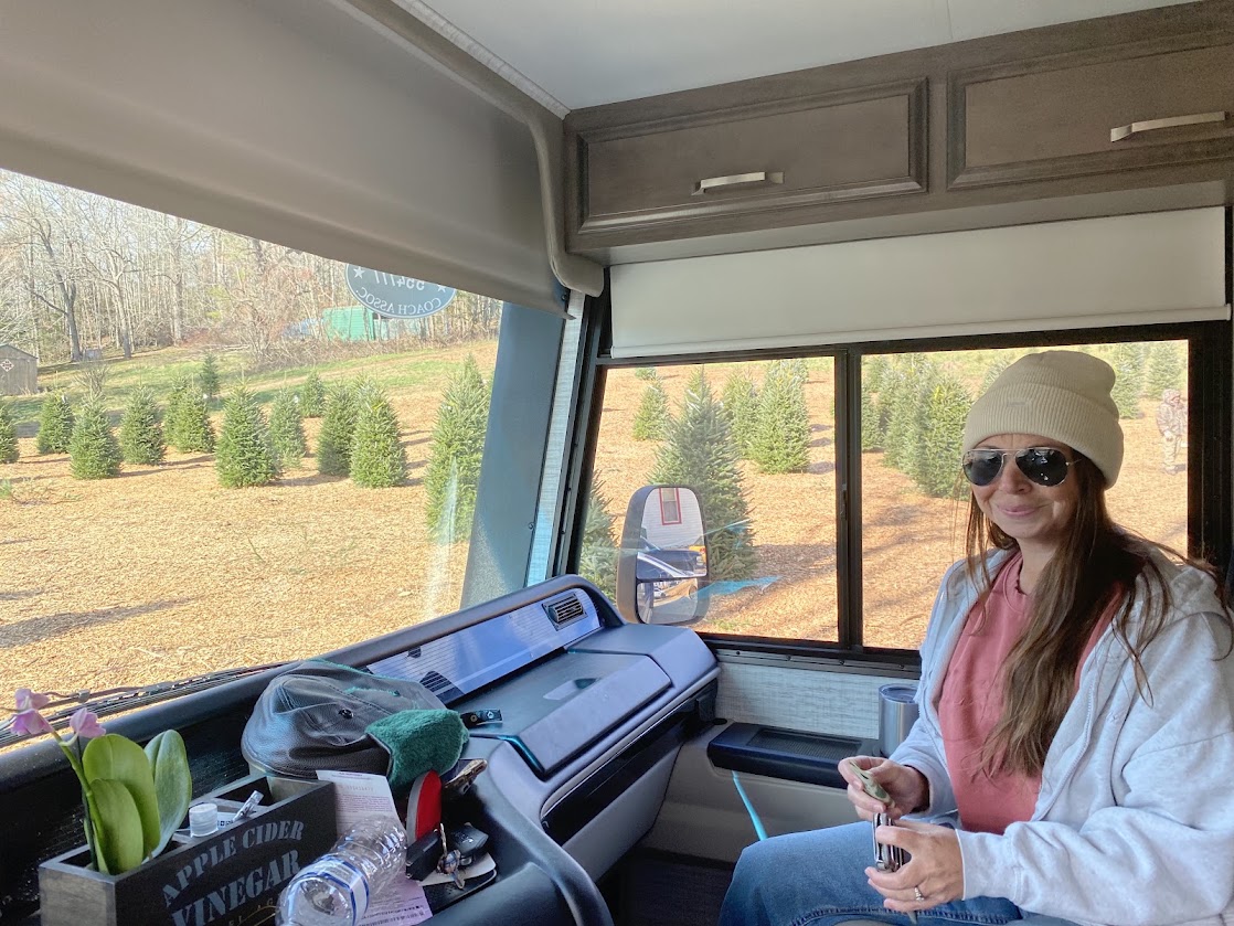 A woman sits at the front of an RV with a view of the tree farm outside.