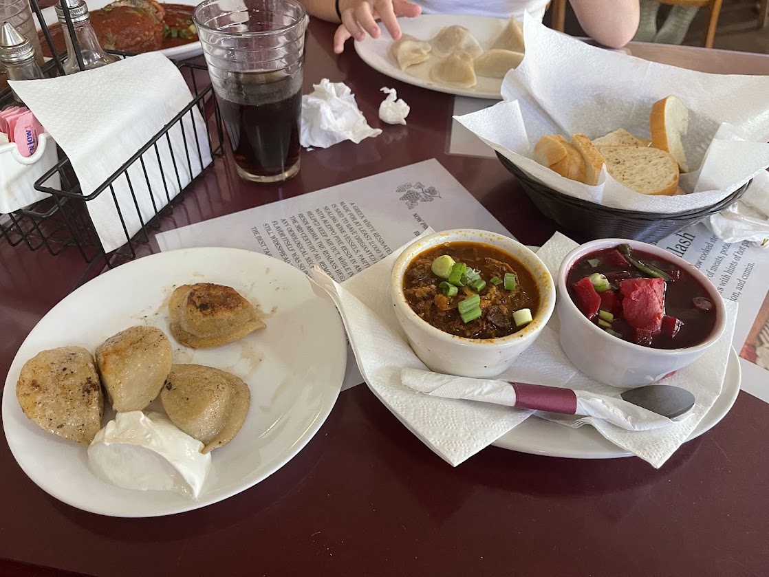 A plate with dumplings, a dipping sauce, and two bowls of soup on a restaurant table.
