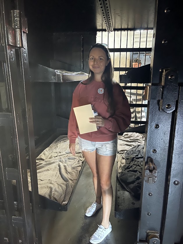 A person holds a paper while standing inside a dark jail cell.