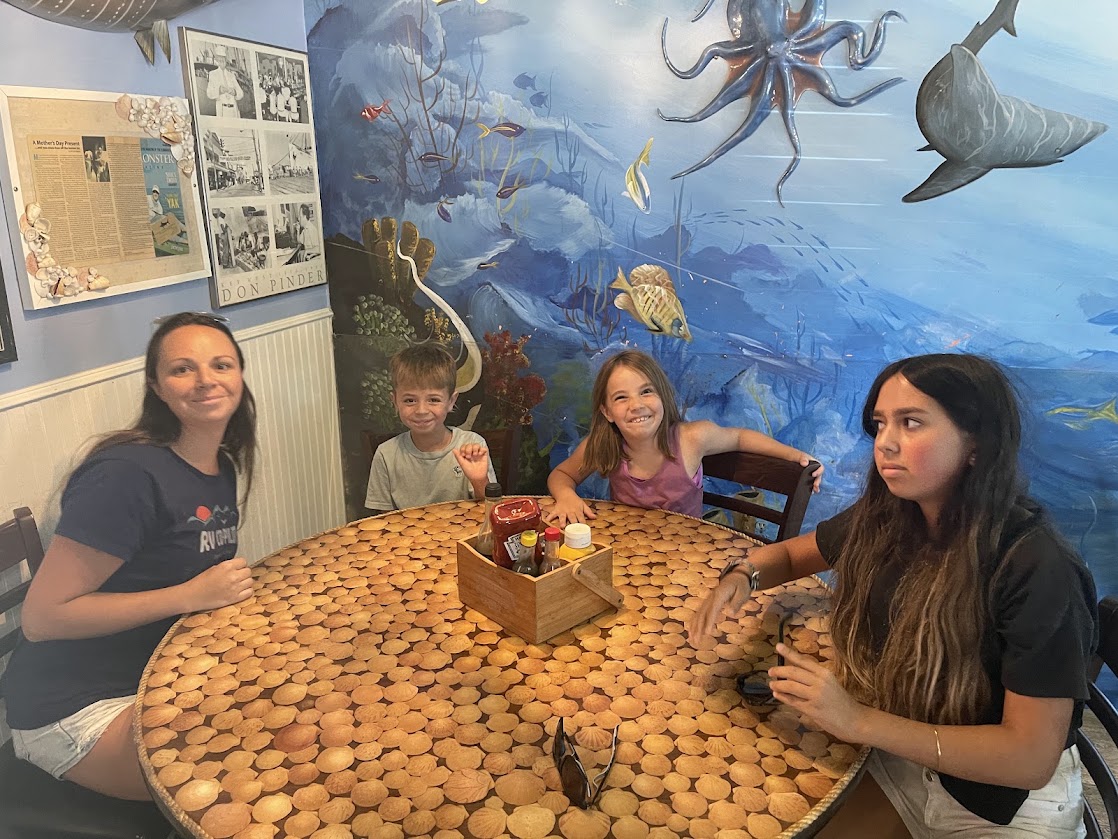 Four people sitting at a round table with a seafood mural behind them.