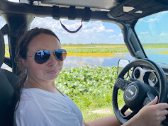 A woman with sunglasses sitting in a vehicle with a water view.
