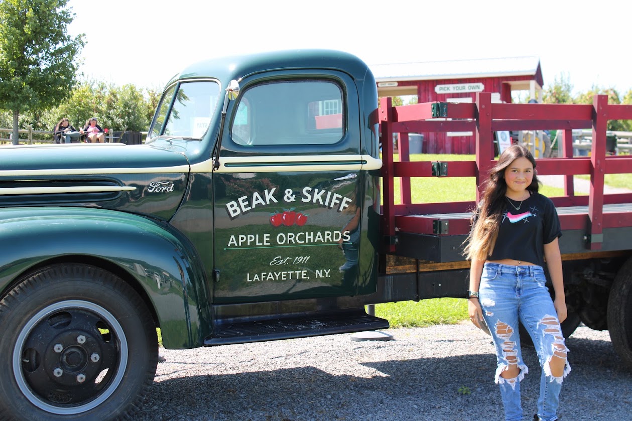 A vintage green truck with Beak and Skiff branding next to a girl.