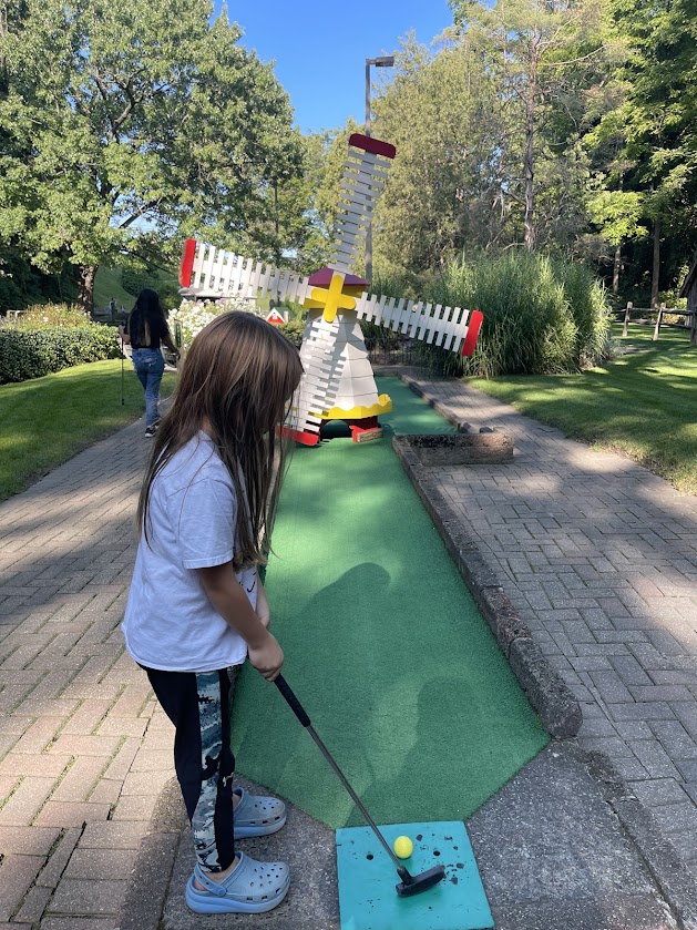 A child prepares to putt near a colorful windmill on the mini golf course.