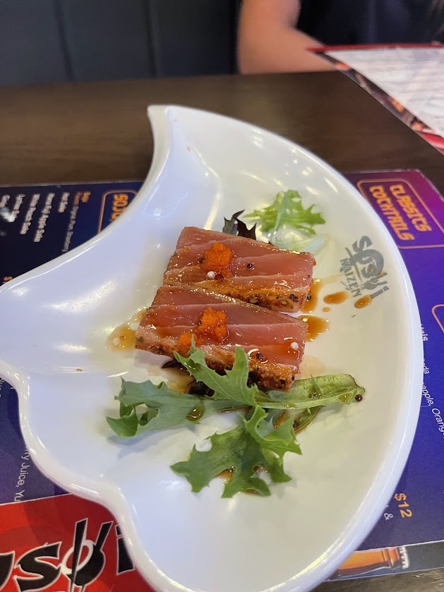 Three pieces of tuna sushi garnished with orange roe, served on a white plate.
