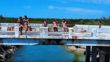 Children and teens sitting on a weathered bridge over turquoise water.