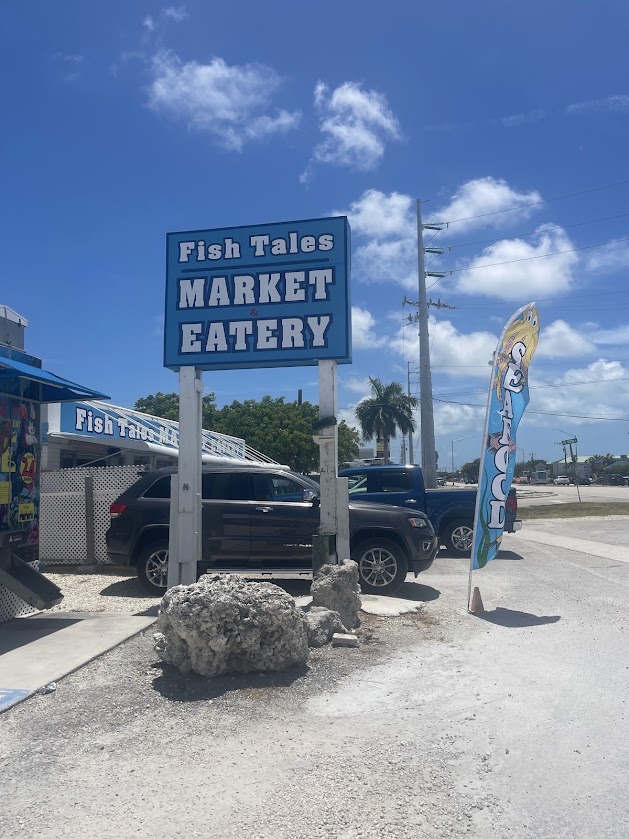 Sign for Fish Tales Market and Eatery under a blue sky in Marathon, Florida.