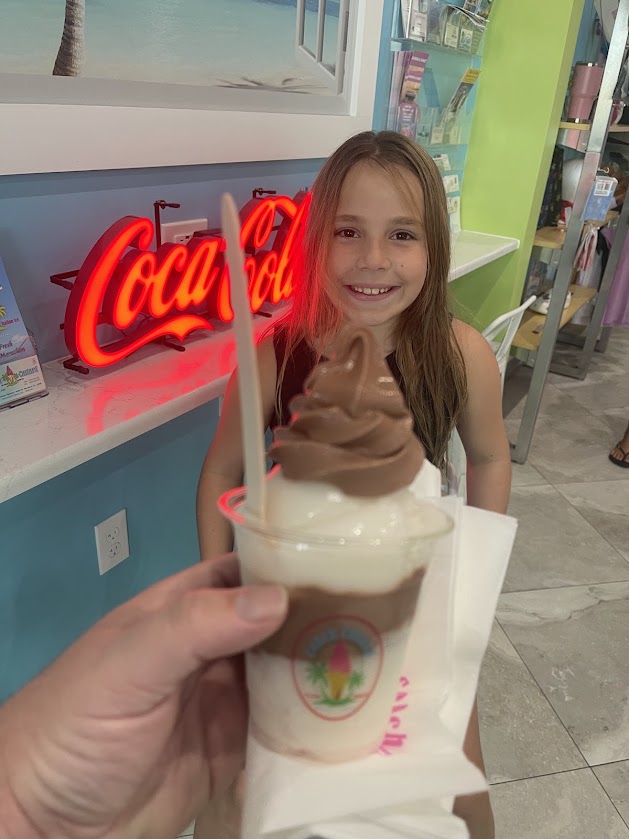 A child smiles while holding a soft serve dessert in a cozy restaurant setting.