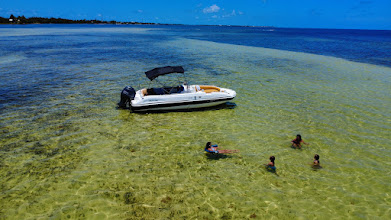 A white boat anchored in shallow water with four people swimming nearby in Layton, Florida.