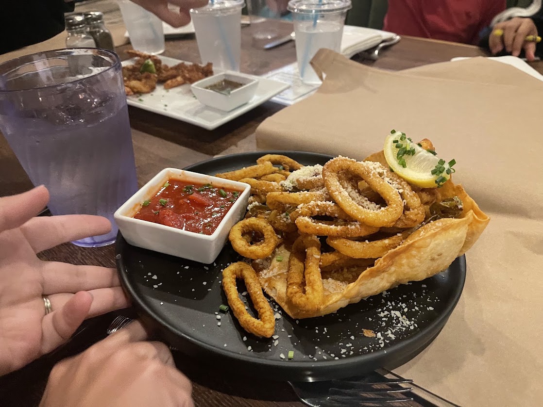 A plate of fried calamari with dipping sauce and a lemon wedge.