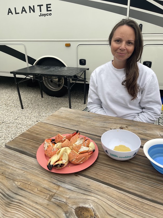 A woman sits at a table with a plate of crab claws and a small bowl.