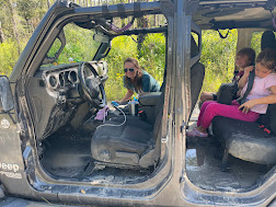 Interior of a muddy Jeep with two children sitting and a woman leaning over the front seat.