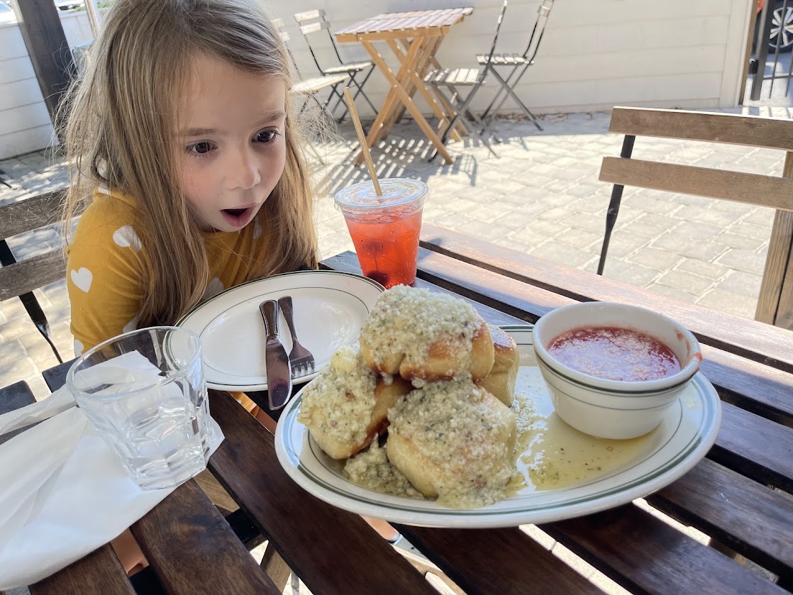 A surprised child looks at a plate of cheesy garlic bread and marinara sauce.