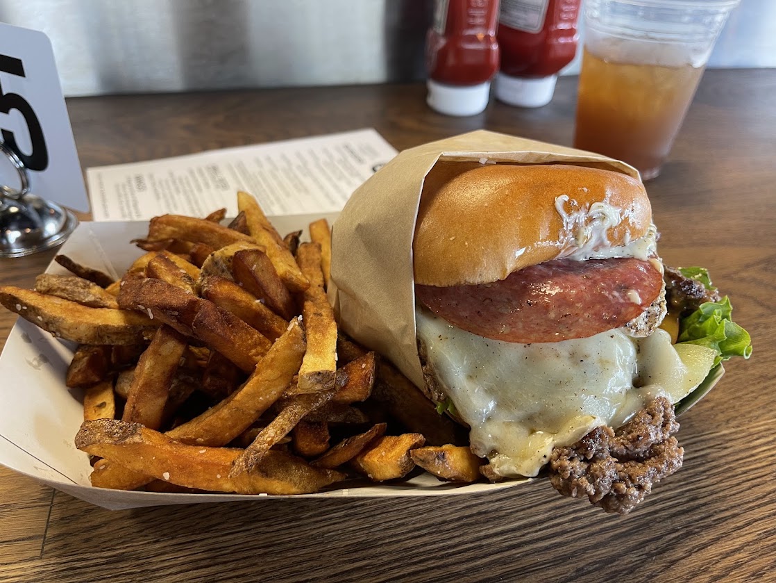 A burger with lettuce, cheese, and salami, served with crispy French fries.
