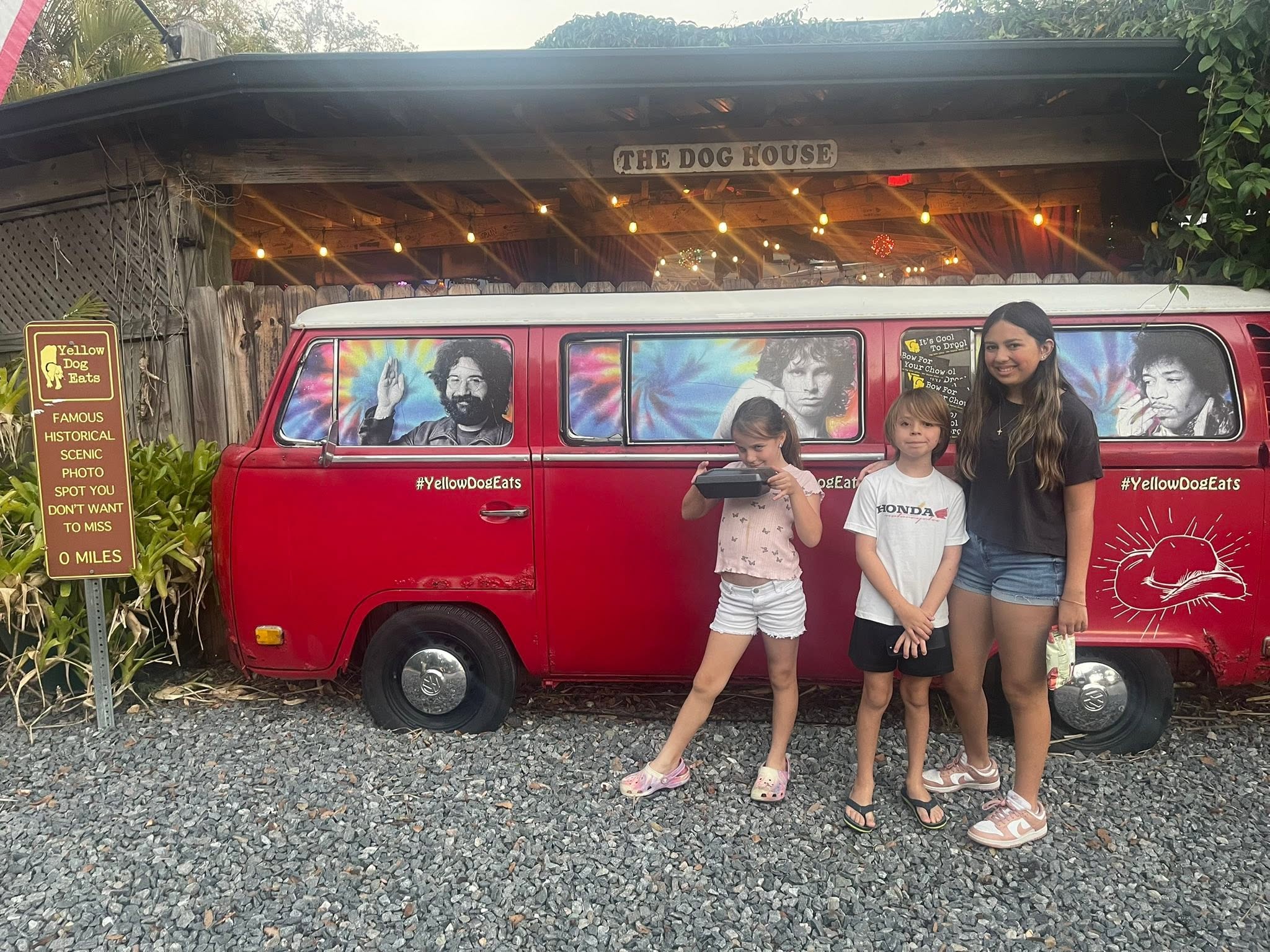 Three children pose by a red vintage van with artistic portraits in front of Yellow Dog Eats.