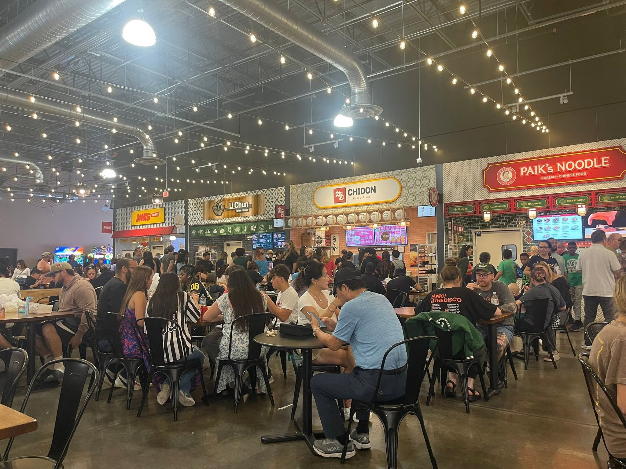 A busy food hall with various dining options and patrons seated at tables.