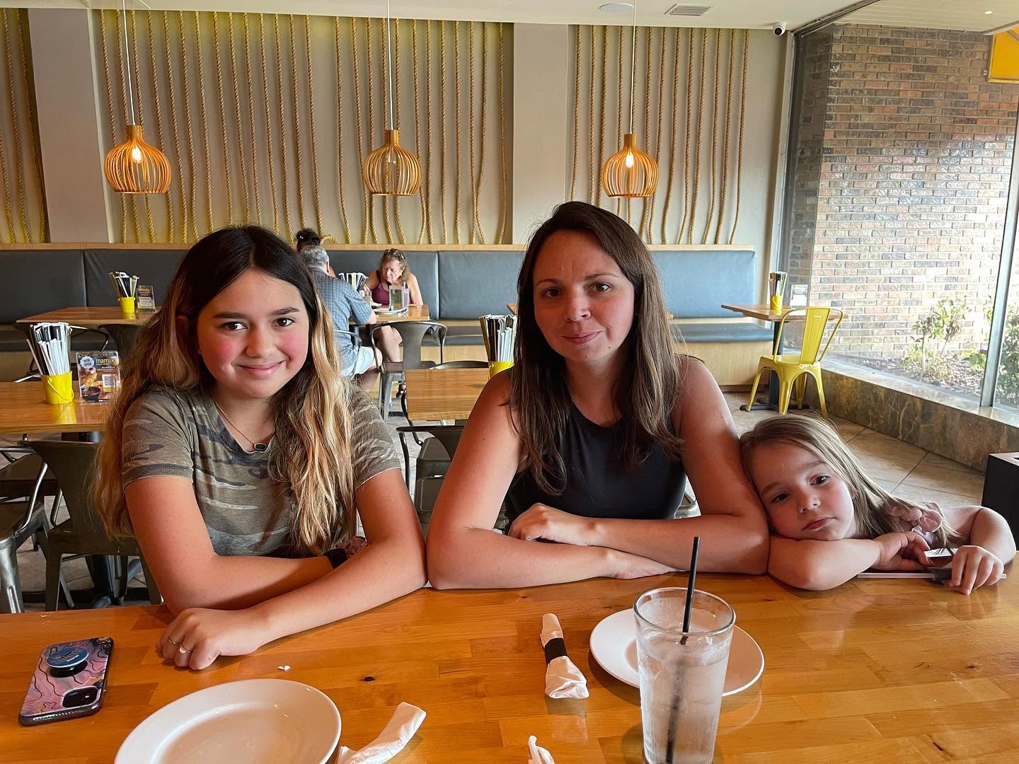 A woman sits with two girls at a wooden table in a restaurant.