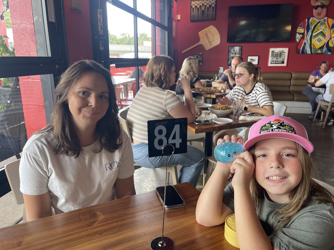 A woman and a child at a table with a number sign, surrounded by diners at Pigzza.